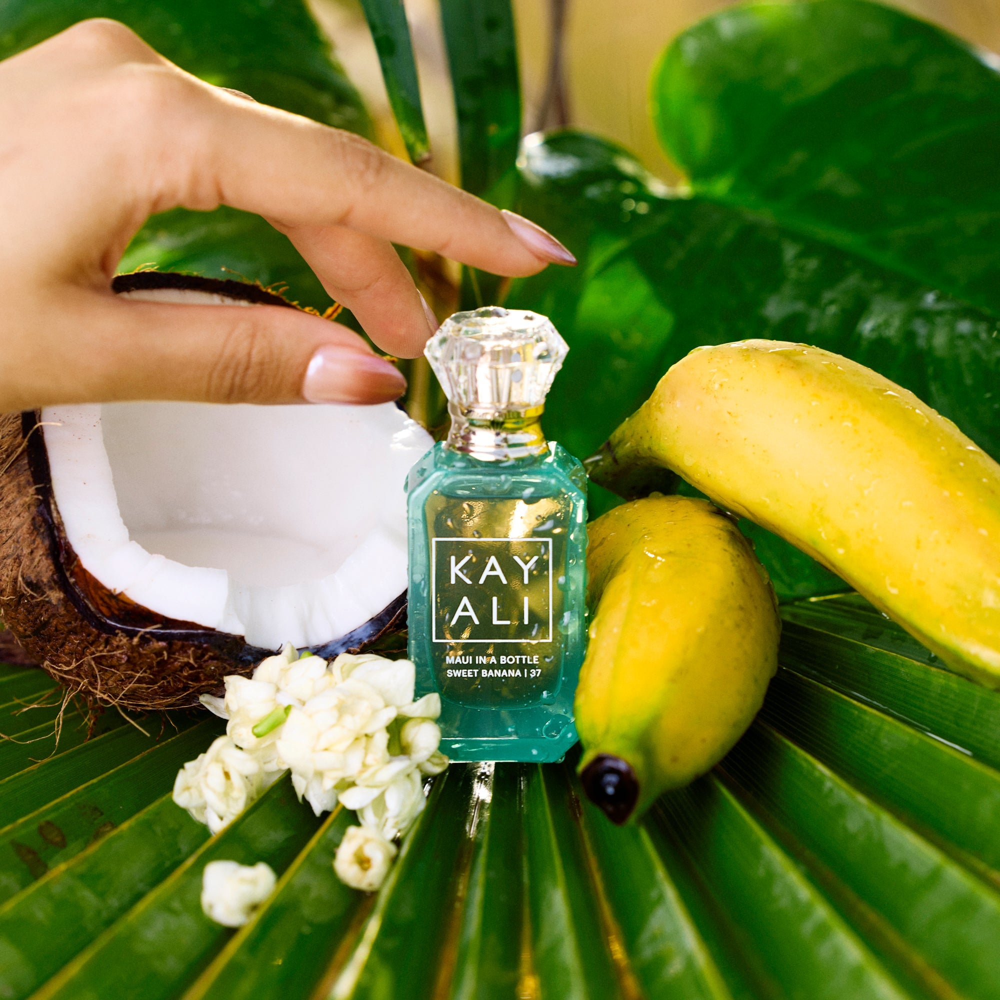 Small bottle of KAYALI perfume on a leaf with bananas and flowers